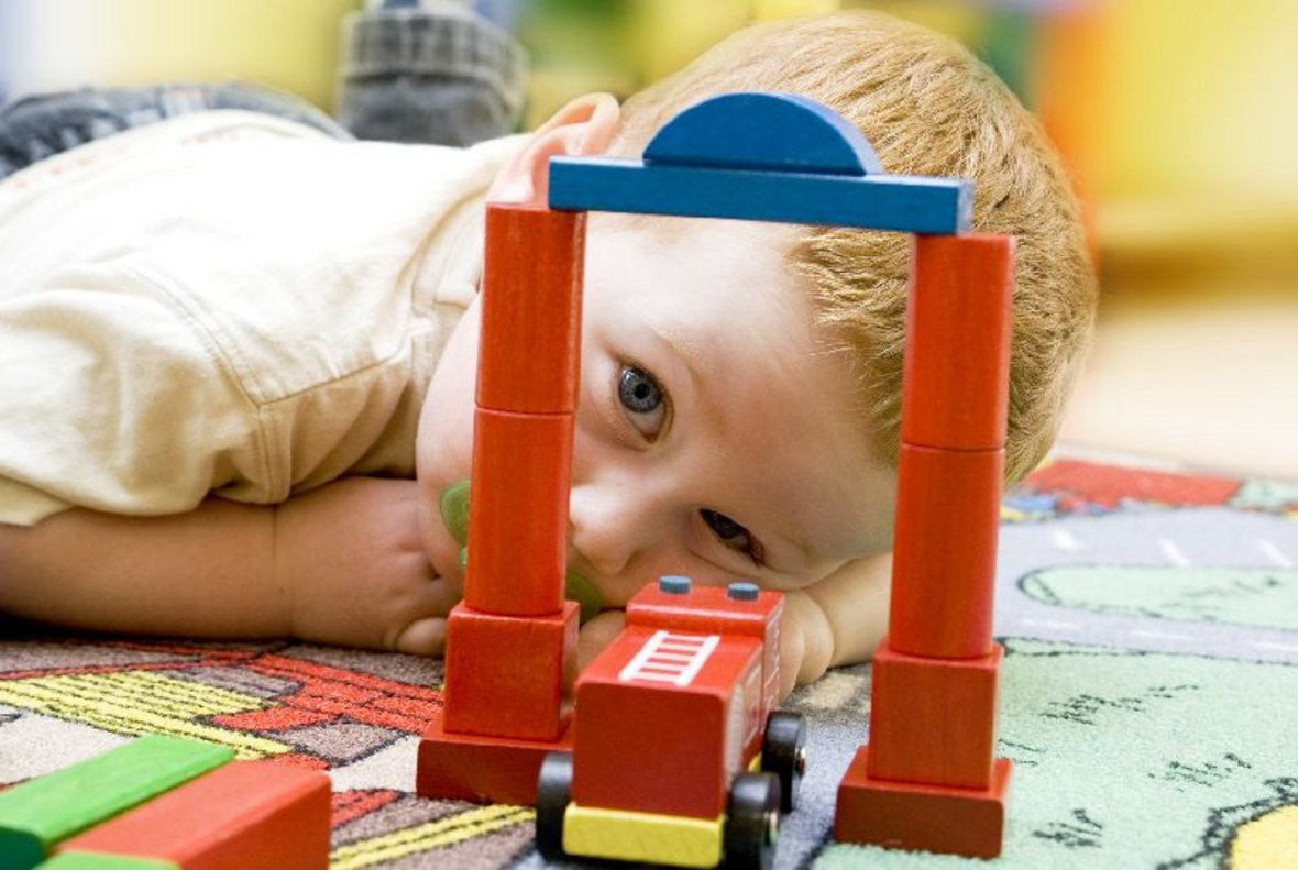 Kind beim Spielen auf dem Boden mit Bauklötzen und Fahrzeugen