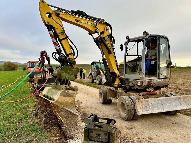Bagger auf einem Feldweg beim Verlegen von Leerrohren